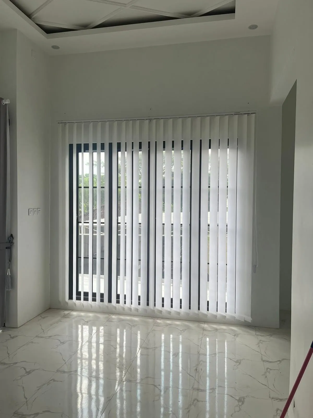 Vertical blinds warna putih bersih terpasang rapi pada jendela kaca besar berbingkai hitam